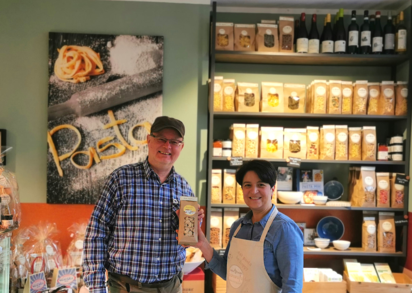 Patric Blies links, Tina Bonaffini Caputo rechts im Bild, beide stehen vor einem Regal im Laden voller Nudeln und halten ihr neues Produkt in den Händen.