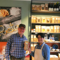 Patric Blies links, Tina Bonaffini Caputo rechts im Bild, beide stehen vor einem Regal im Laden voller Nudeln und halten ihr neues Produkt in den Händen.